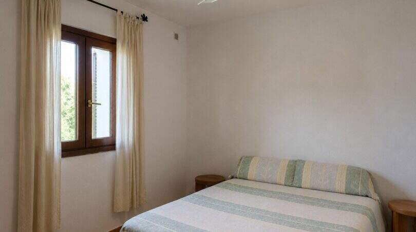 Helles Schlafzimmer der Finca Lloseta mit Doppelbett, Deckenventilator und Fenster mit Gardinenschmuck.