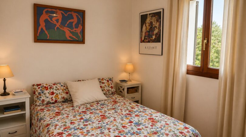 Dormitorio luminoso de la finca Lloseta con cama doble, colcha con flores, grabados artísticos y ventanas de madera con vista al jardín.