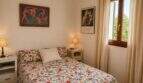 Helles Schlafzimmer der Finca Lloseta mit Doppelbett, Blumendecke, Kunstdrucken und Fenster zum Grün.