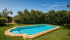 Piscina exterior de la finca mallorquina en Lloseta, rodeada de césped verde y árboles mediterráneos.