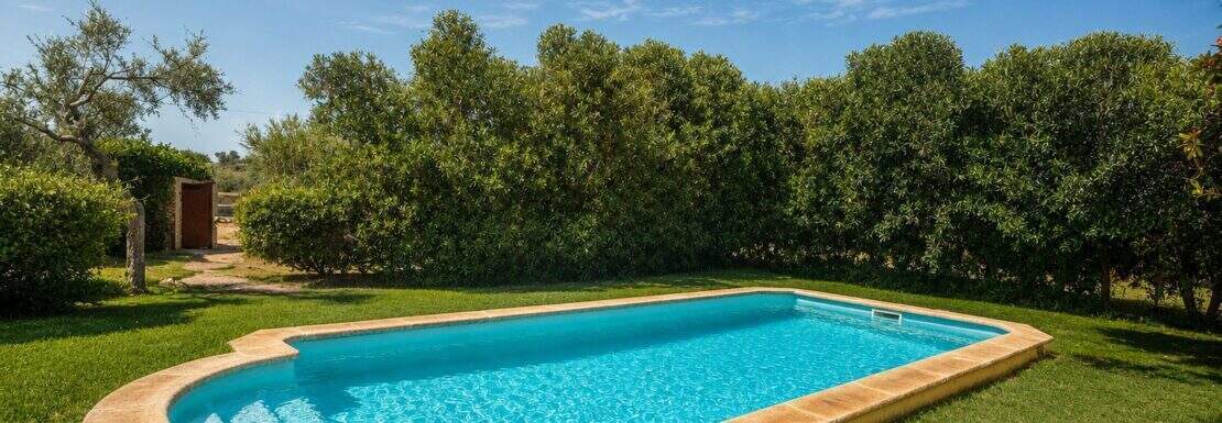 Private pool with a natural stone edge, surrounded by the lush greenery of the Mallorcan finca in Lloseta