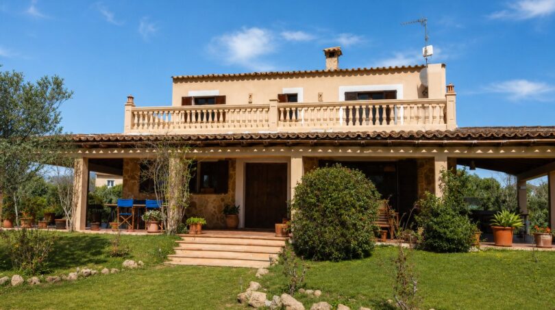 Vista exterior de la finca mallorquina en Lloseta con balcón, terraza y jardín bien cuidado.