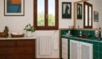 Baño de la finca Lloseta con azulejos verdes, lavabo rojo, cómoda de madera y encanto rústico.