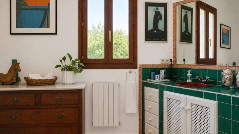 Baño de la finca Lloseta con azulejos verdes, lavabo rojo, cómoda de madera y encanto rústico.