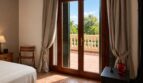 Dormitorio de la finca Lloseta con puerta a la terraza, suelo de piedra natural y vista a palmeras y balcón