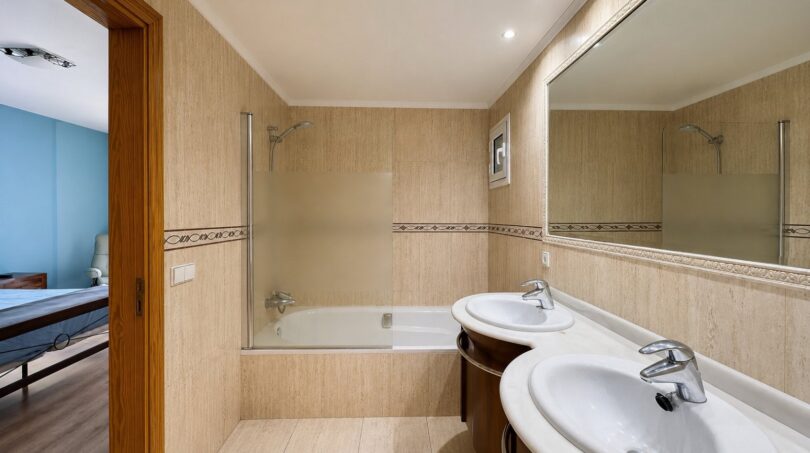 Baño luminoso de la dúplex en Sa Torre con lavabo doble, bañera y ducha, revestimiento de azulejos de color beige.