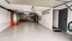 Garaje doble espacioso con suelo de resina epoxi, estanterías, coche clásico rojo y puerta de acceso a la casa en Sa Torre