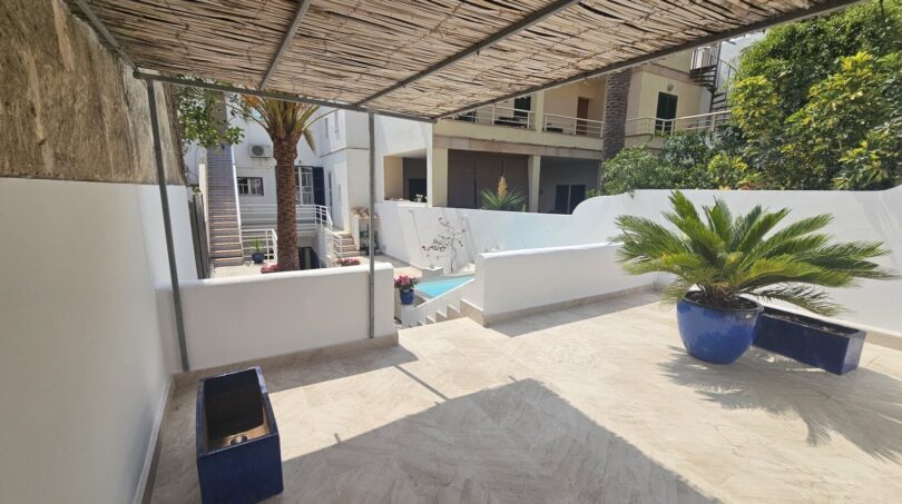 Covered terrace with pool, palm trees and blue ceramic pots of a modern apartment in Portocolom