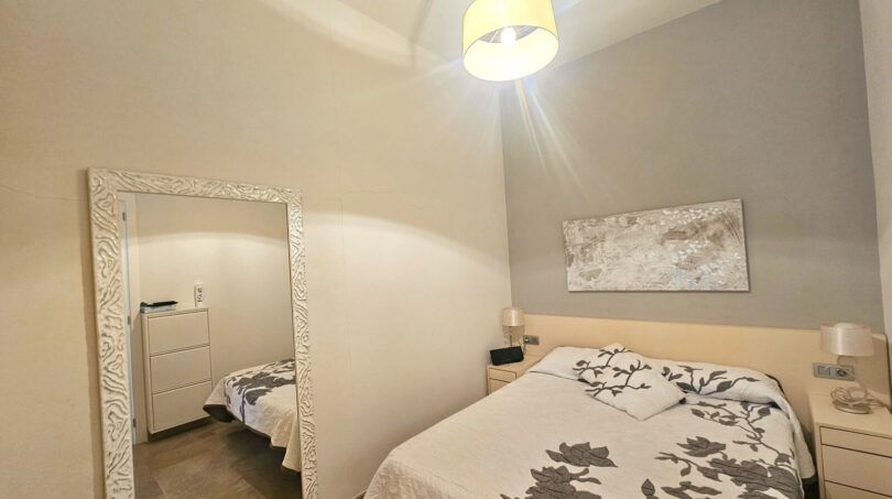 Bright bedroom with double bed, gray wall design, large mirror and pendant light in Portocolom apartment