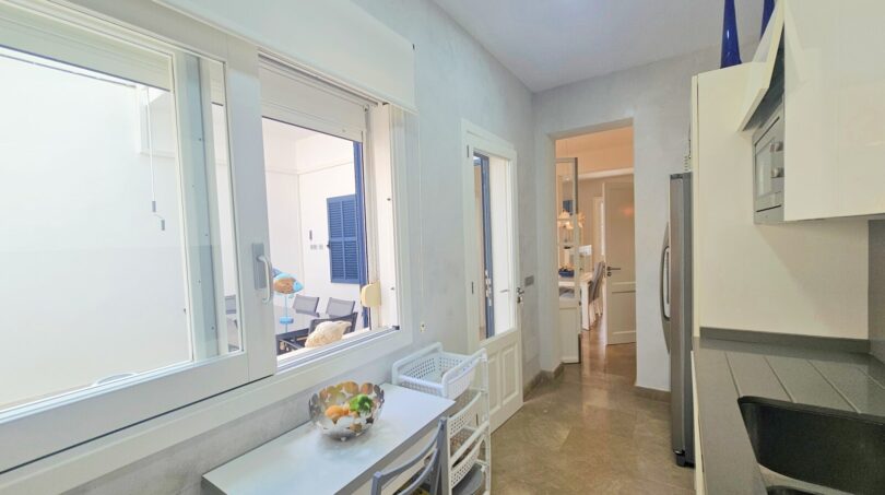Bright kitchen with small dining table, window to terrace, modern appliances and passage to living area in Portocolom