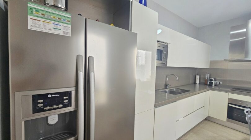 Modern white fitted kitchen with stainless steel side-by-side refrigerator and integrated appliances in Portocolom apartment