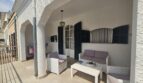 Covered terrace with white rattan furniture, arch passage and dark shutters in Portocolom
