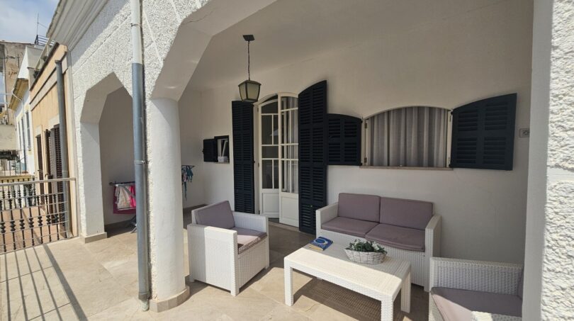 Covered terrace with white rattan furniture, arch passage and dark shutters in Portocolom