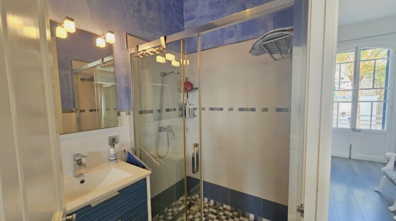 Modern bathroom with glass shower, blue-white tiles and washbasin in the apartment in Portocolom