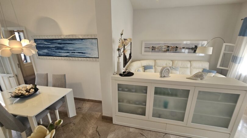 Bright living room with white sideboard, leather sofa and dining table in modern apartment in Portocolom