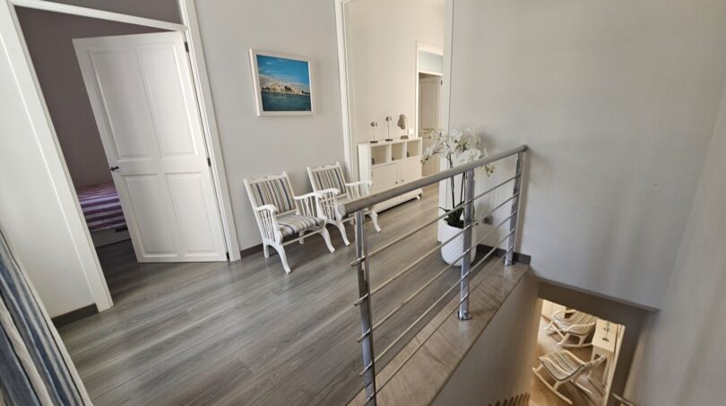 Bright stairwell with chrome railing, wooden floorboards and seating area in modern apartment in Portocolom