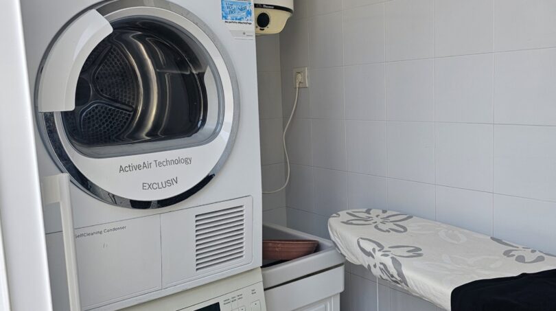Utility room with stacked washing machine and dryer plus ironing board in modern apartment in Portocolom