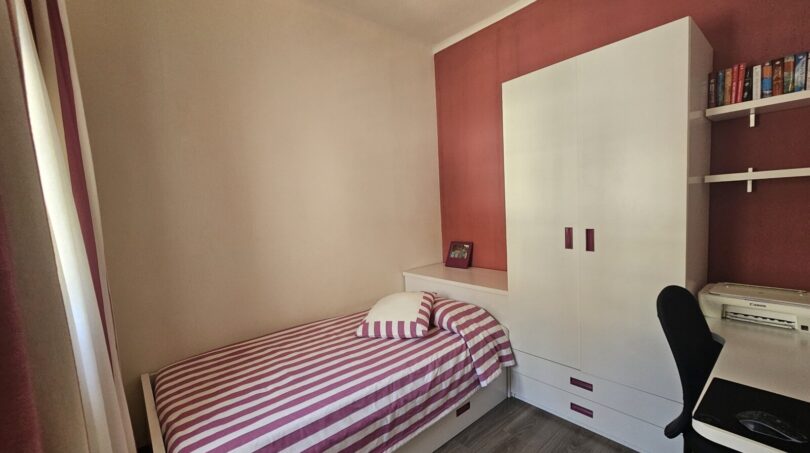 Small bedroom with single bed, white wardrobe and desk, red accent wall, Portocolom apartment