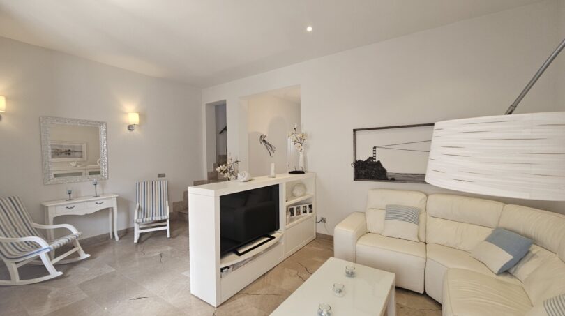 Bright living room with white leather sofa, TV unit and marble floor in modern apartment in Portocolom