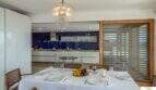 Elegante comedor con lámpara de cristal, mesa dispuesta y cocina moderna en villa de lujo Cala Magrana