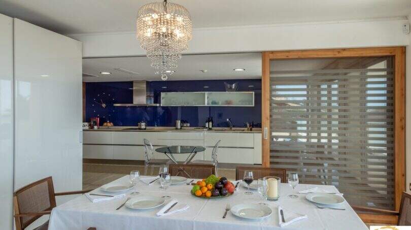 Elegante comedor con lámpara de cristal, mesa dispuesta y cocina moderna en villa de lujo Cala Magrana