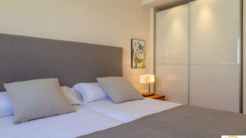 Elegante dormitorio de la villa de lujo en Cala Magrana con cama doble, armario empotrado y lámpara de mesilla