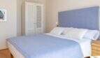 Dormitorio luminoso de la villa de lujo en Cala Magrana con cama doble, cabecero tapizado azul y armario empotrado blanco.
