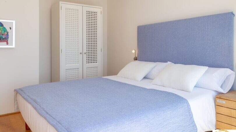 Dormitorio luminoso de la villa de lujo en Cala Magrana con cama doble, cabecero tapizado azul y armario empotrado blanco.