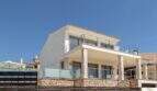 Villa de lujo mediterránea Cala Magrana: Fachada exterior blanca con balcón de cristal, muro de piedra natural y terraza en primera línea de mar.