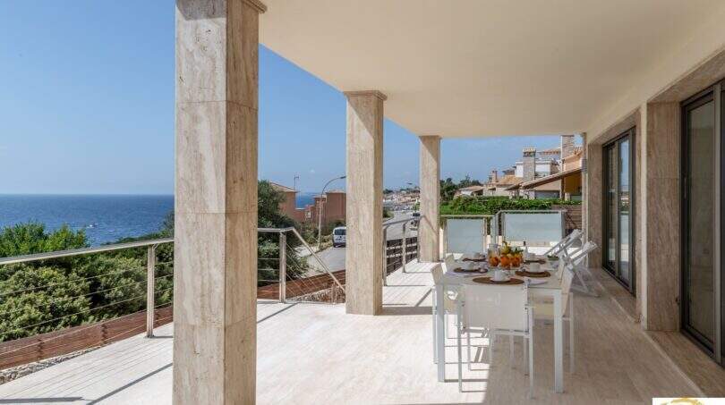 Terraza cubierta con columnas de mármol, conjunto de comedor blanco y vistas al mar de la villa de lujo en Cala Magrana