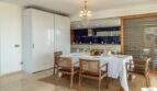 Elegante comedor con lámpara de cristal, mesa dispuesta y cocina de diseño abierta de la villa de lujo en Cala Magrana.