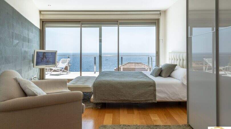 Dormitorio luminoso de la villa de lujo en Cala Magrana con cama doble, suelo de madera y terraza con vistas al mar.