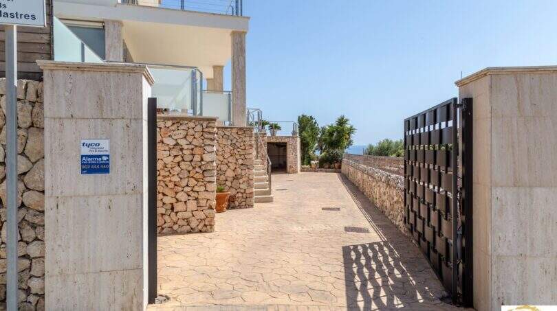 Entrada de la villa de lujo en Cala Magrana con muros de piedra, puerta moderna y vistas al mar de fondo.