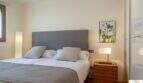 Elegante dormitorio de la villa de lujo en Cala Magrana con cama doble, cabecero tapizado gris y mesilla de madera