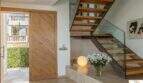 Zona de entrada de la villa de lujo en Cala Magrana con escalera de madera, barandilla de cristal y elegante suelo de piedra natural.
