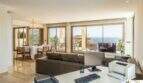 Sala de estar luminosa con vistas al mar, zona de trabajo, comedor y lámpara de araña en villa de lujo Cala Magrana