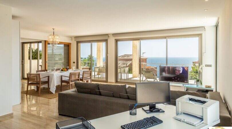 Sala de estar luminosa con vistas al mar, zona de trabajo, comedor y lámpara de araña en villa de lujo Cala Magrana