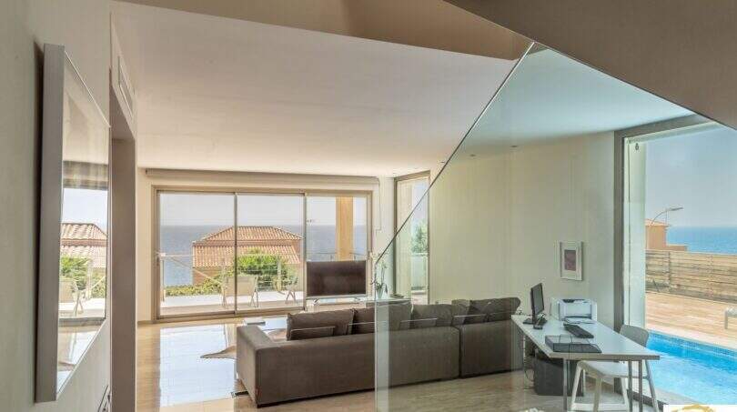 Sala de estar moderna de la villa de lujo en Cala Magrana con barandilla de cristal, piscina y vistas al mar