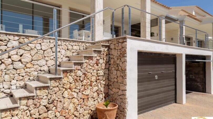 Entrada y escalera exterior de una villa de lujo mediterránea en Cala Magrana con muro de piedra natural y garaje doble.