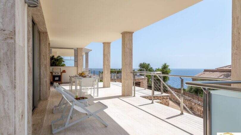 Amplia terraza de la villa de lujo en Cala Magrana con vistas al mar, tumbonas y columnas de piedra natural.