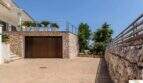 Entrada con muro de piedra natural, garaje y terraza con palmeras de la villa de lujo en Cala Magrana