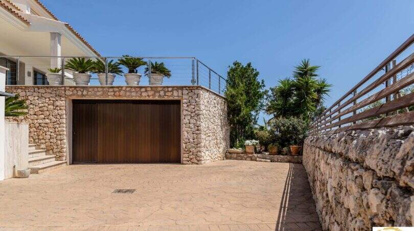 Entrada con muro de piedra natural, garaje y terraza con palmeras de la villa de lujo en Cala Magrana