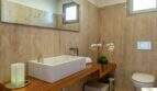 Elegante baño de la villa de lujo con paredes de travertino, lavabo sobre encimera y WC suspendido en pared
