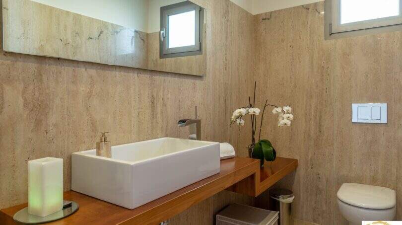 Elegante baño de la villa de lujo con paredes de travertino, lavabo sobre encimera y WC suspendido en pared