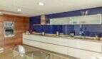 Cocina de lujo moderna con salpicadero de cristal azul, frentes de alto brillo blancos y elementos de madera en Villa Cala Magrana