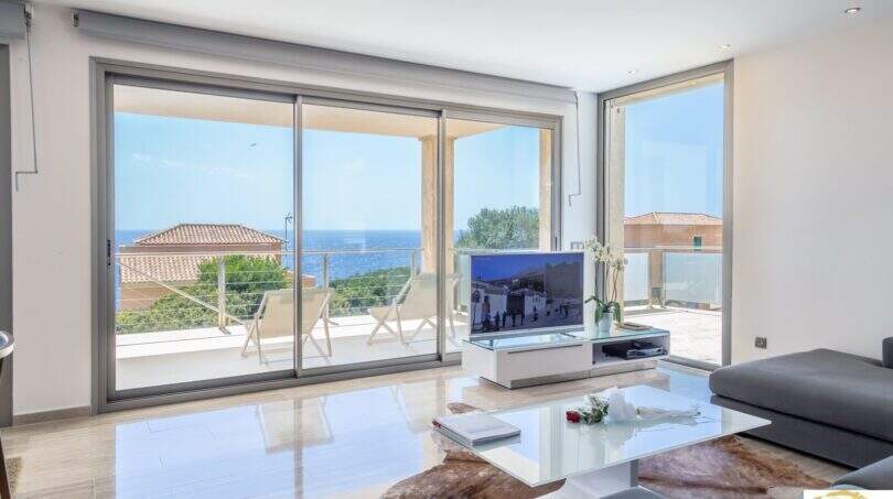 Sala de estar luminosa de la villa de lujo en Cala Magrana con acristalamiento panorámico y vistas espectaculares al mar