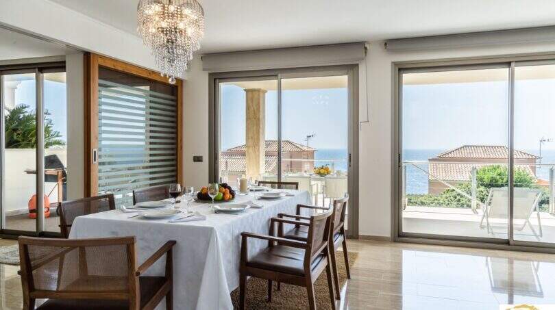 Elegante comedor de la villa de lujo en Cala Magrana con lámpara de cristal y vistas panorámicas al mar