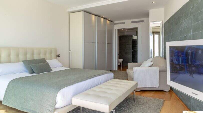 Dormitorio luminoso de la villa de lujo con cama doble, armario empotrado, televisor Samsung y baño en suite en Cala Magrana.