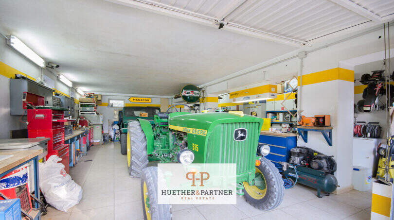 Werkstattgarage der Finca Son Macià mit John-Deere-Traktor, Werkzeugwänden und gelbem Wanddekor
