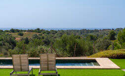 Infinity-Pool mit Holzliegen, Meerblick und üppiger Natur der Finca in Cales de Mallorca